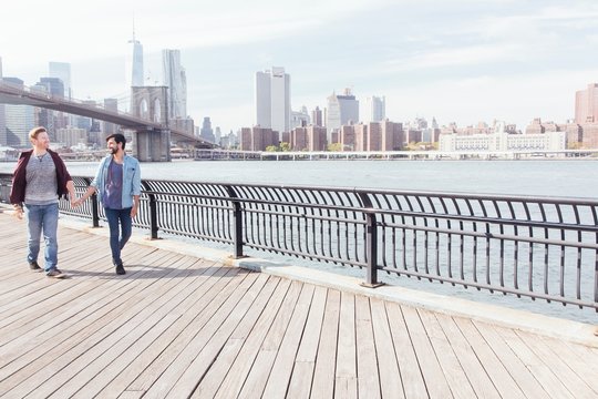 Male couple strolling on riverside by Brooklyn Bridge, New York, USA