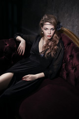 Sexy young woman in black dress lying on red vintage couch