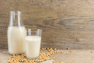 Bottle and glass of soy milk with soybeans, on wooden background