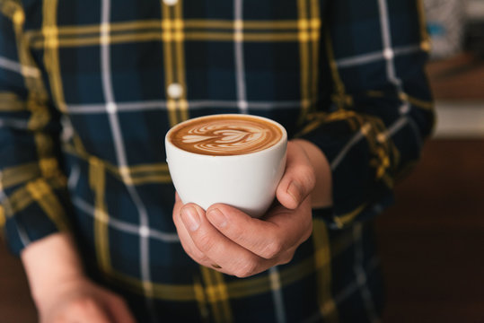 Cropped shot of man wearing checked shirt holding cup of latte