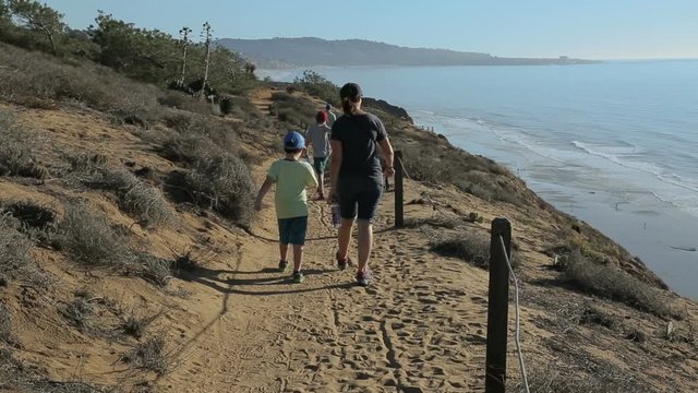 A family with a mother and her children hike on a trail above the ocean.