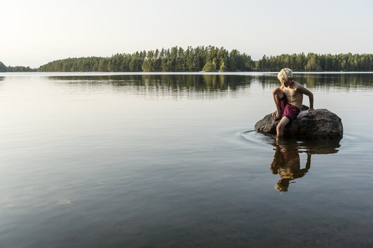 Shirtless boy sitting on rock in lake