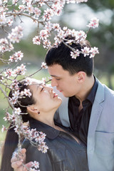 Fototapeta premium Asian girl and european guy kissing among of blossoming almond b