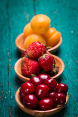 Fresh cherries,strawberries and apricots in a bowl on wooden green table.