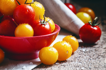 Red and orange cherry tomatoes in a red bowl, vintage wooden bac