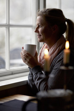 Woman holding coffee cup and looking through window