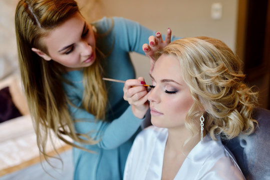Wedding makeup artist making a make up for bride. Beautiful sexy model girl indoors. Beauty woman with curly hair. Female portrait. Bridal morning of a cute lady. Close-up hands near face