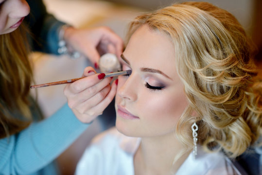 Fototapeta Wedding makeup artist making a make up for bride. Beautiful sexy model girl indoors. Beauty woman with curly hair. Female portrait. Bridal morning of a cute lady. Close-up hands near face