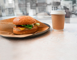 Unhealthy food concept, burger and hot coffee drink in takeaway cup on table in cafe, a lot of space for text on foreground, copyspace, toned image.