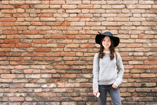 Beautiful asian girl in fashionable dress, standing in front of red brick wall background with copy space