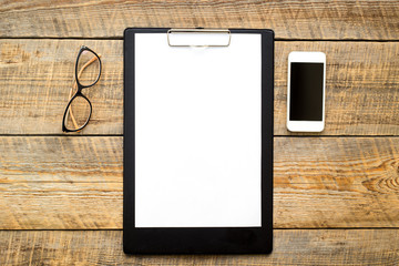 blank sheet on wooden table with glasses and smartphone