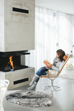 Woman reading book in front of fireplace