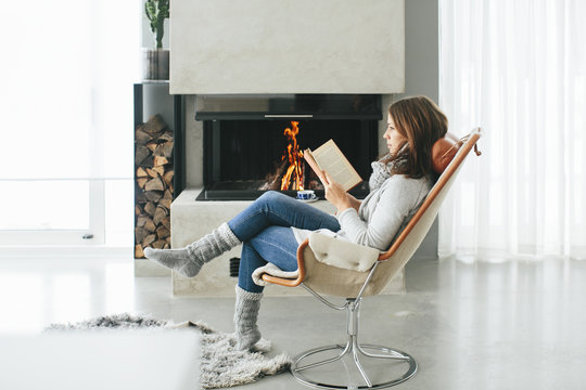Woman reading book in front of fireplace