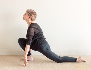 Older woman in black yoga clothing in lunge yoga posture on floor