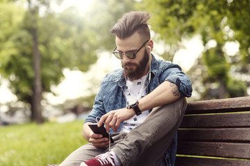 Young bearded fashionable man typing on cell phone