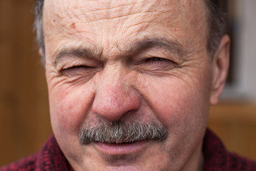Elderly man with disdain looking at the camera, wrinkles his nose and forehead
