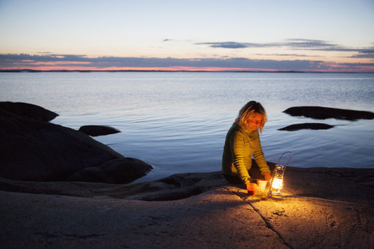 Woman sitting with lantern on lakeshore