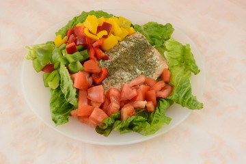 Salmon salad with lettuce, tomatoes and red, green and yellow bell peppers on plate on tablecloth