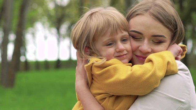 Little girl embracing mother and kissing her in park. Slowly