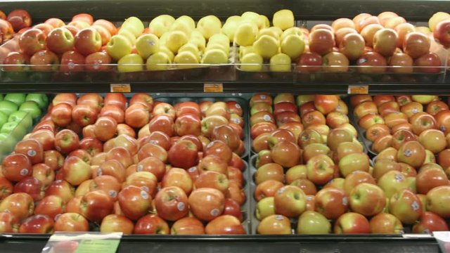 Tracking shot (dolly) past fresh fruit in a supermarket grocery. Includes red apples, green apples, lemons, etc.