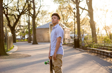 Hispanic skateboarder stands in the park looking far out over th