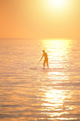 Woman paddle boarding on the sea at stunning orange sunset