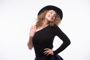 woman with curly hair in black hat and stylish elegant evening dress posing on white studio background.