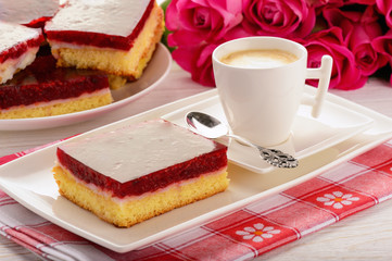 Piece of biscuit cake with cream and cherry jelly and cup of coffee.
