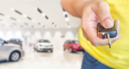 hand of man with car key on blur photo car showroom