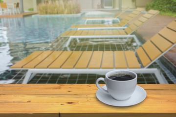 Cup of coffee on the wooden floor and Blurred swimming pool back