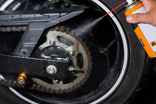Fototapeta Cleaning and oiling a motorcycle chain and gear with oil Spray.