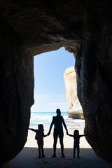 Fototapeta premium Sylwetka matki z dwójką dzieci w jaskini na plaży Tunnel w pobliżu Dunedin w Nowej Zelandii