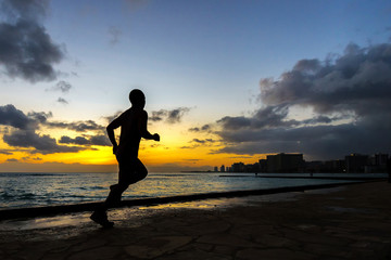 Fototapeta na wymiar Silhoutte of runner jogging along Waikiki beach at sunset golden hour