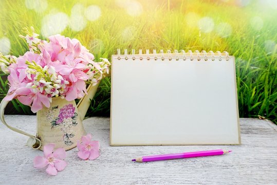 Fototapeta pink flower on wooden table in soft pastel tone of bokeh nature green grass, including blank page paper of calendar, pencil, spring morning sunlight background