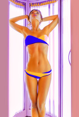 Slim young woman standing in solarium getting sun tan