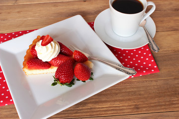 Erdbeeren, ein Stück Erdbeerkuchen mit Sahne auf weißem eckigem Teller mit einer Tasse Kaffee - Strawberrycake
