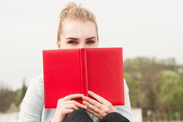 Close-up portrait of beautiful woman hiding behind red book