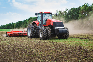 Moderne tech rode tractor ploegen een groen landbouwveld in het voorjaar op de boerderij. Maaimachine die tarwe zaait.