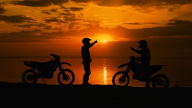 Two motorcyclists at sunset communicate. They are naberegu River, near his motocross bike.