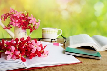 pink flower on wooden table with bokeh nature green grass , including notebook, paper page sunglasses,pen cup of coffee, open book and smart phone, business or technology background 
