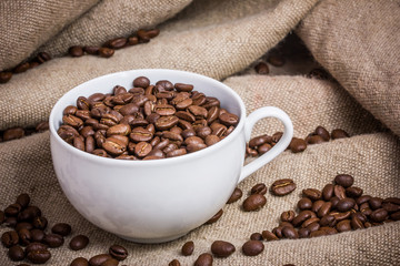 White cup with coffee seeds inside on linen fabric.