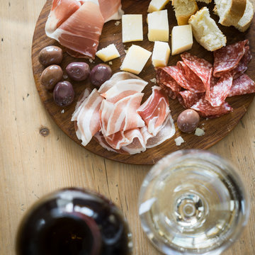 Traditional italian apero: white wine and plate with  prosciutto crudo, salami, parmesan cheese, olives and bread