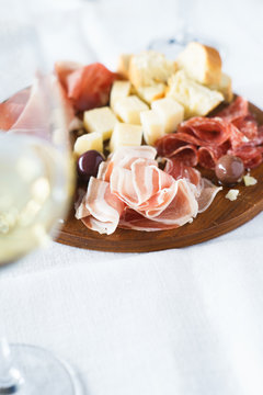 Traditional italian apero: white wine and plate with  prosciutto crudo, salami, parmesan cheese, olives and bread. Selective focus.