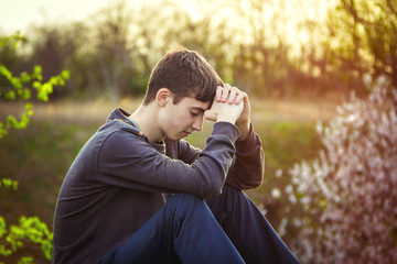 Sad guy sitting alone on the ground with his eyes closed in sunset light, outdoors
