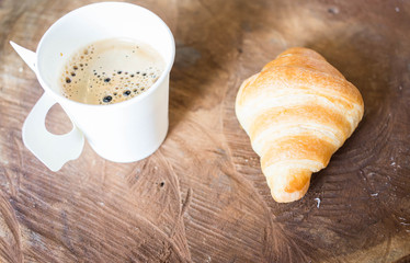 Hot coffee with croissant on wood.