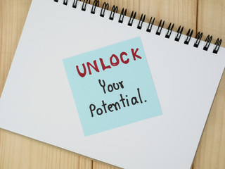 Handwriting Unlock Your Potential on colorful notepaper and notebook with wood background. (Business concept)