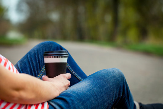 A Girl Sits With The Cup Of Coffee In A Park