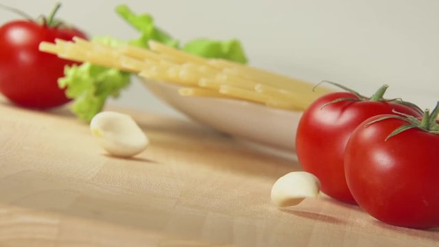 SLOW: A garlic falls on a table near spaghetti and tomatoes