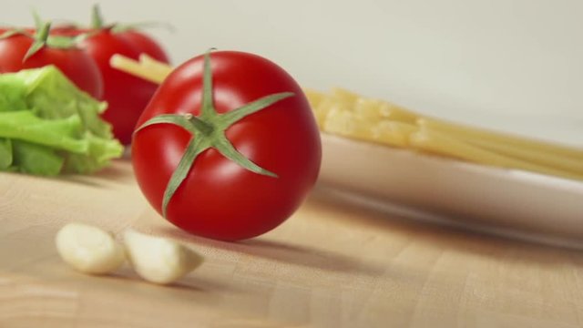 SLOW: A ripe tomato rolls on a table near spaghetti and garlic