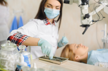 Naklejka na ściany i meble Young beautiful woman dentist doing first check-up for female patient at the dental clinic. Doctor taking dental tools wearing mask and gloves. Medical equipment.